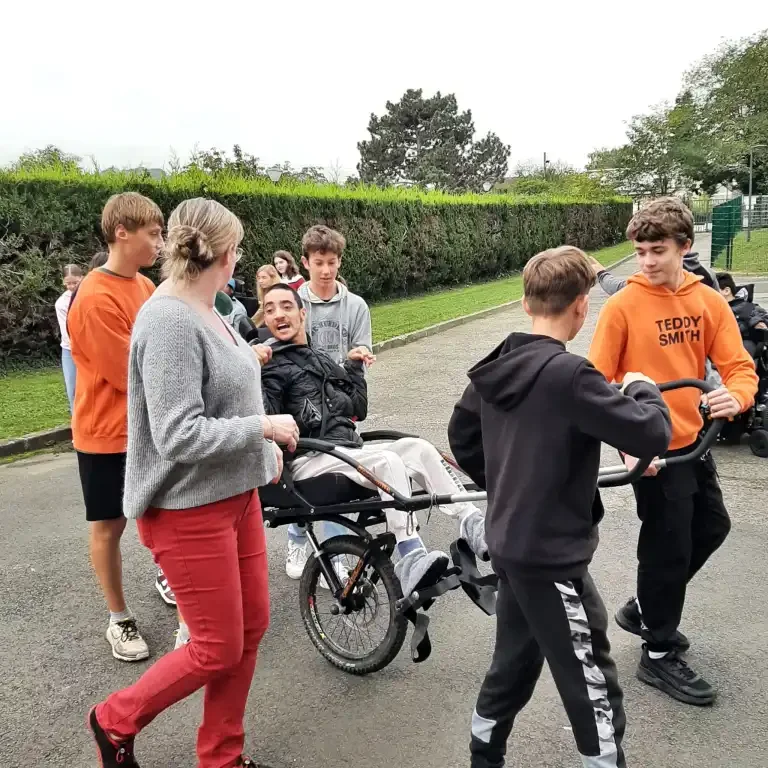Un groupe réuni autour d’une personne installée dans un fauteuil de randonnée, lors d’une sortie en extérieur.